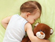 Baby schläft mit Teddy im Arm