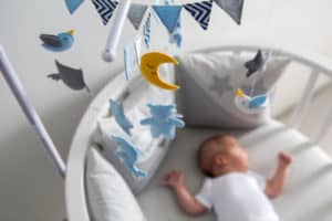 Baby schläft im Babybett und darüber hängt ein Mobile