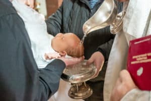 Baby wird bei der Taufe Weihwasser über den Kopf geschüttet